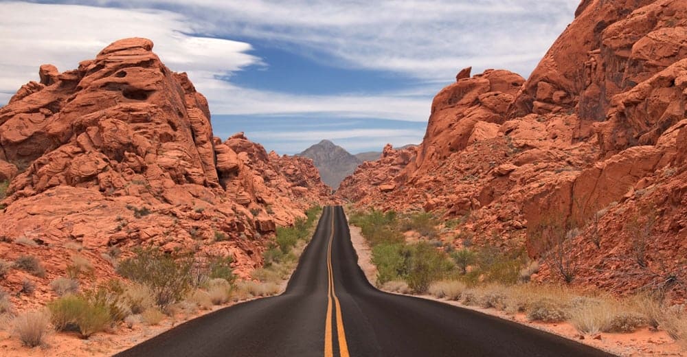 Long empty road through red rock formations in a desert landscape.