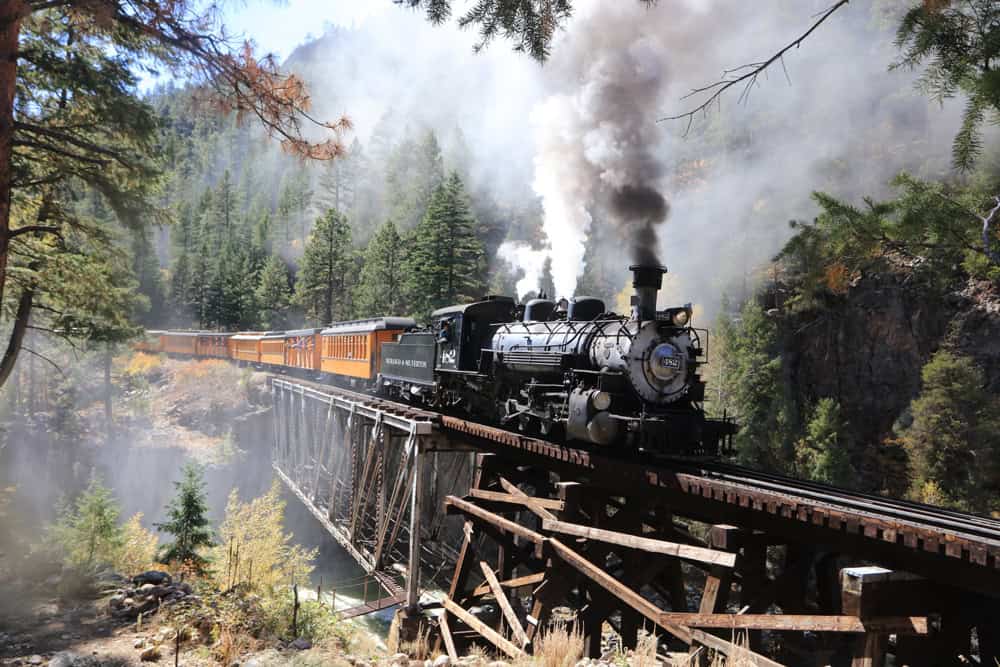 Vintage steam locomotive traveling through lush forest landscape.