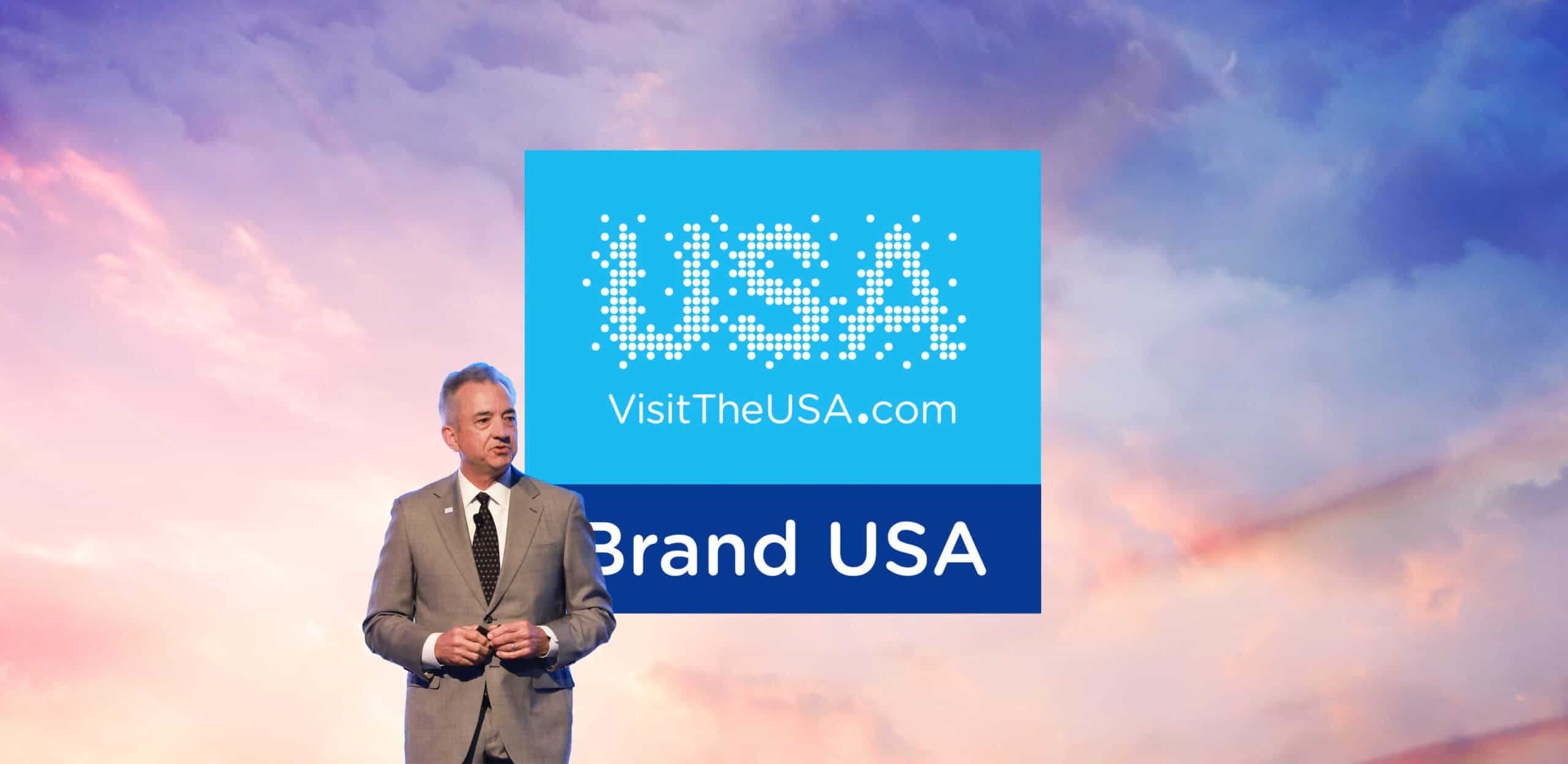 Chris Thompson speaking at Brand USA event with USA tourism logo.