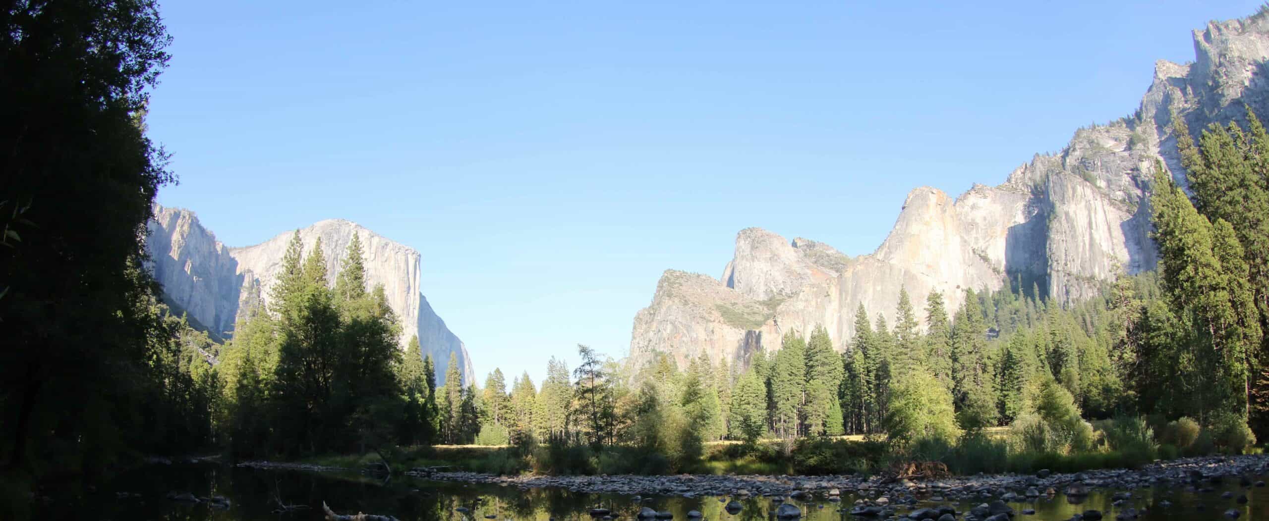 Majestic mountain range with lush green trees and clear blue sky.