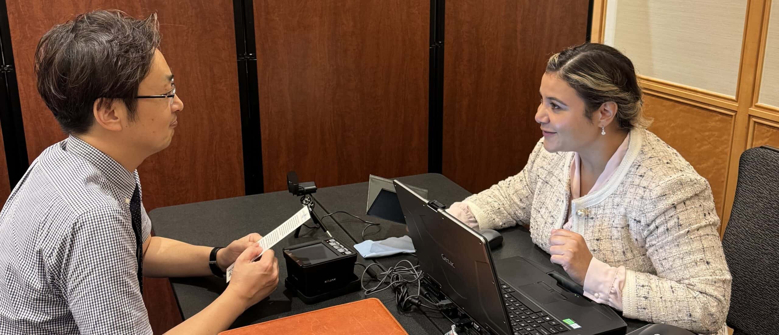 U.S. Customs officer and traveler discussing at a desk in an office.