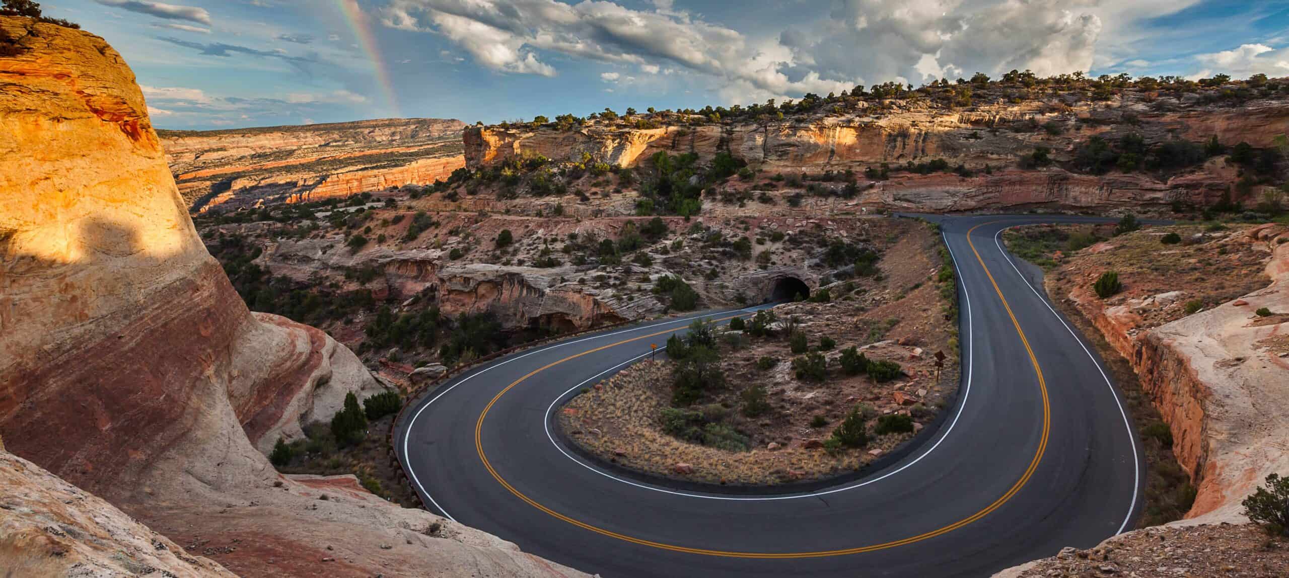 Winding road through a canyon with colorful rock formations and blue sky.