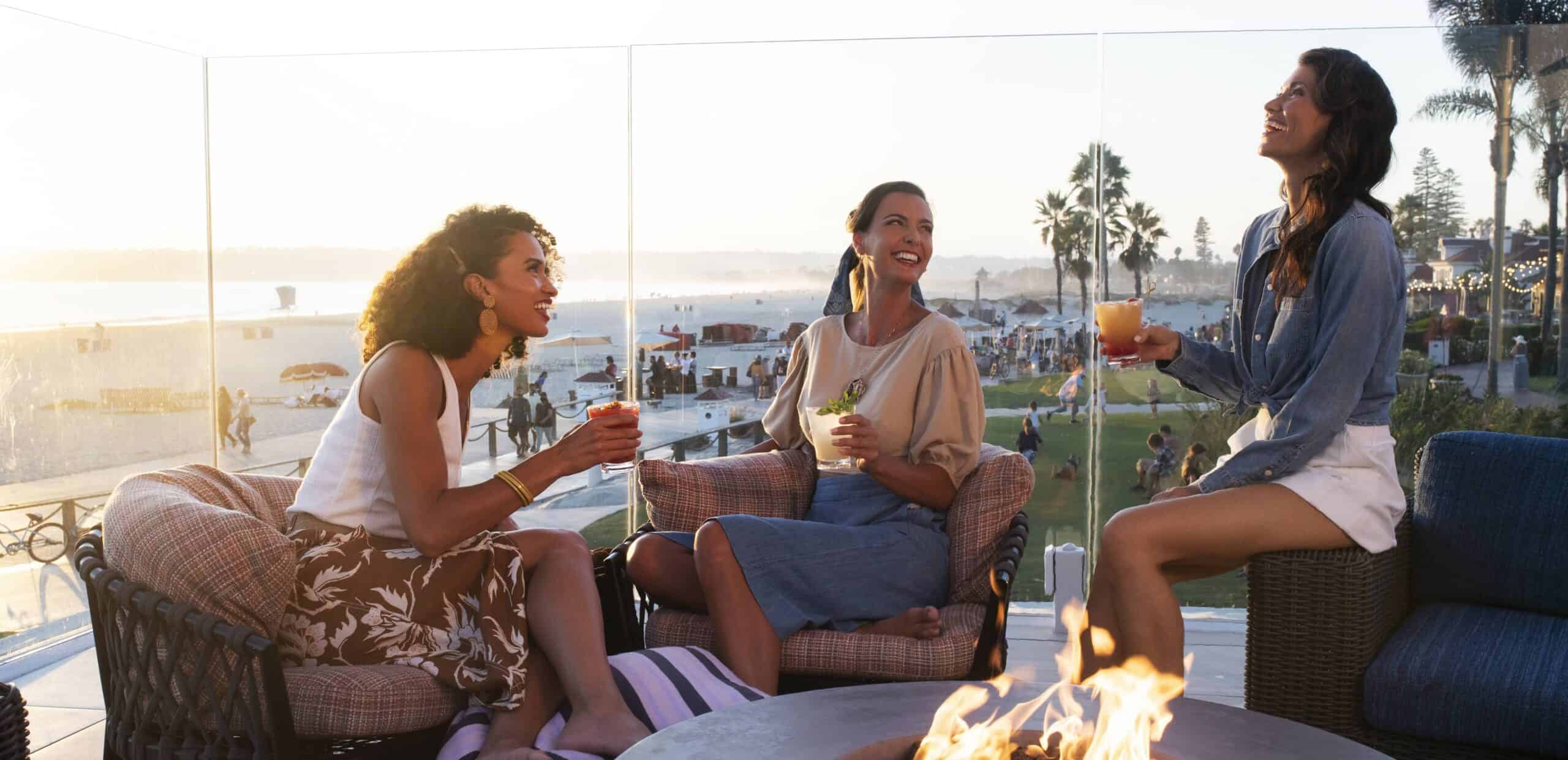Group of women enjoying drinks at sunset with beach view in the background.