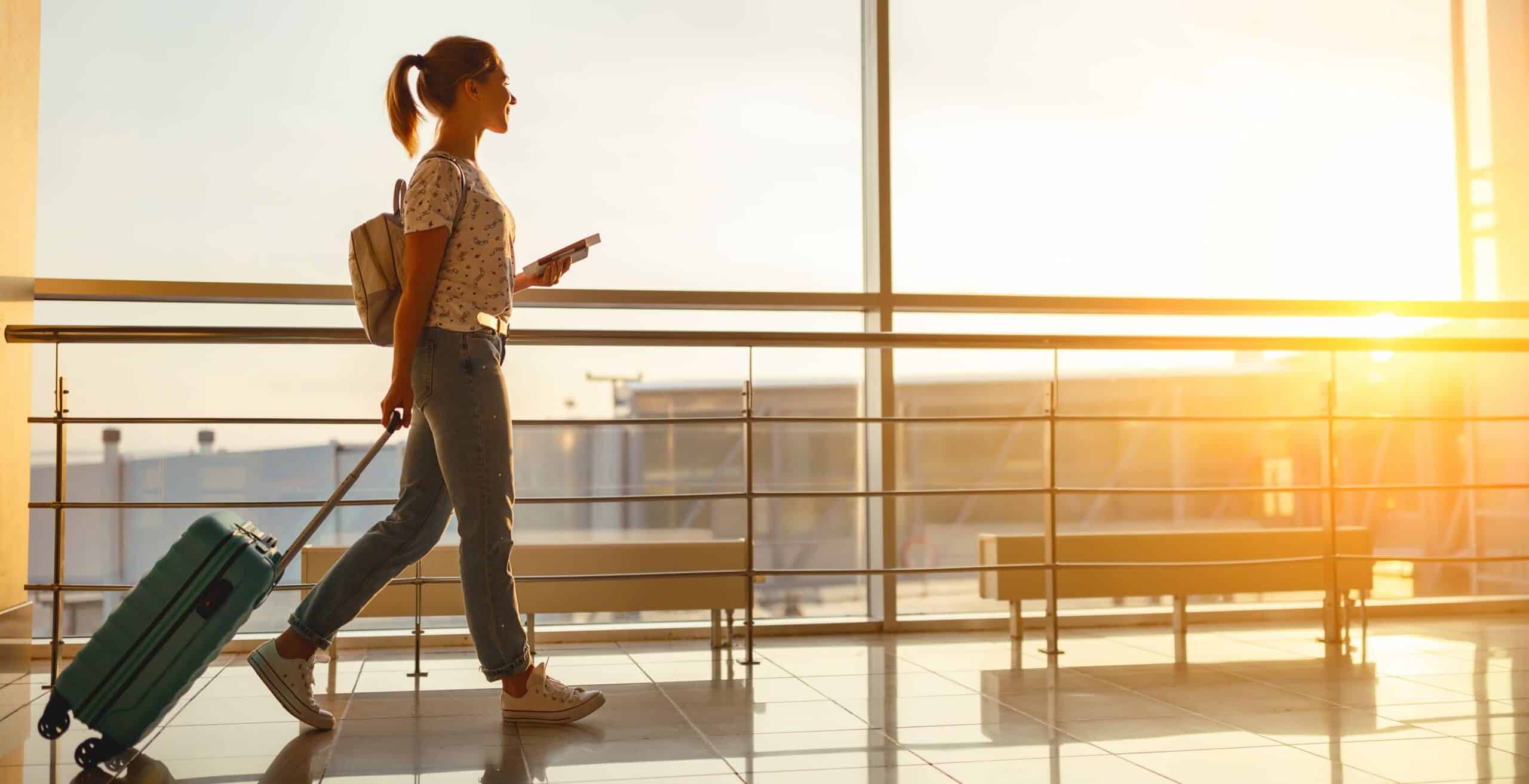 Woman with suitcase walking through airport terminal at sunset.