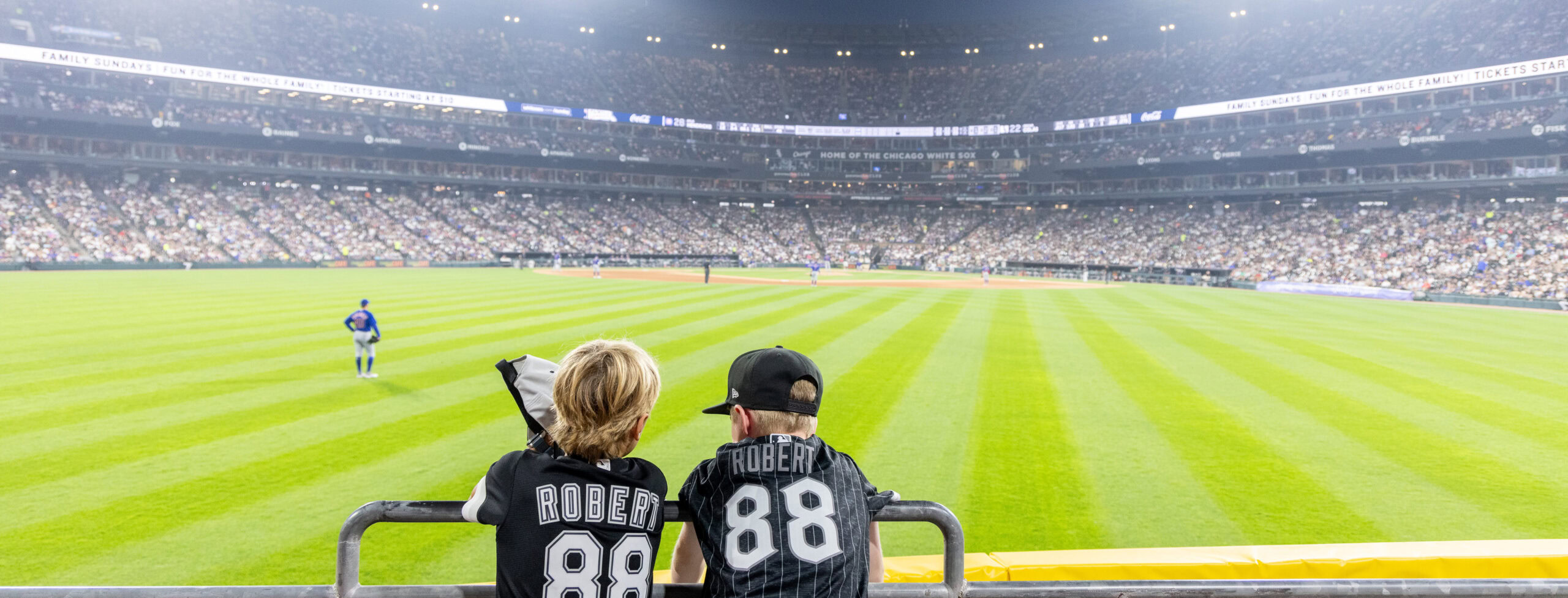 Two children watching a baseball game at a stadium at night.