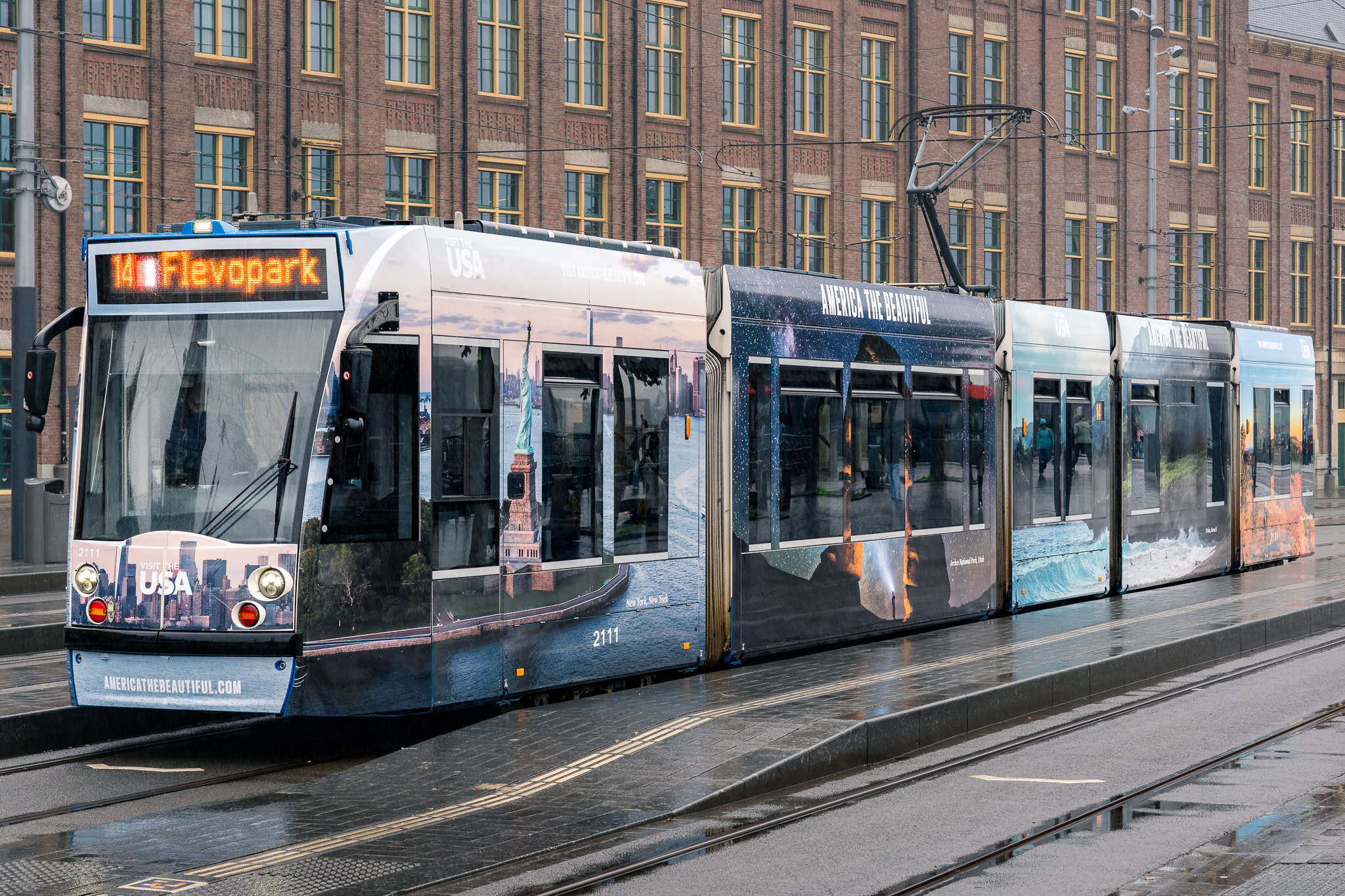 A tram parked at a station featuring “Visit the USA” branding and photographic wraps of American landmarks.